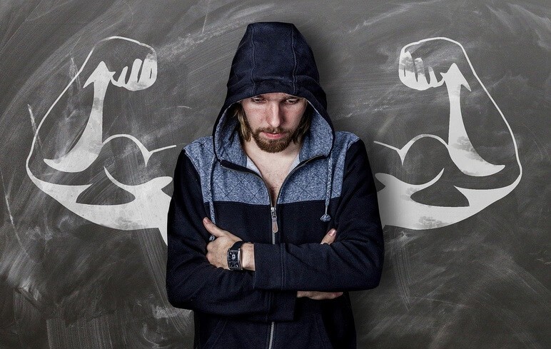 Strong and resilient man in a hoodie with muscled arms behind him